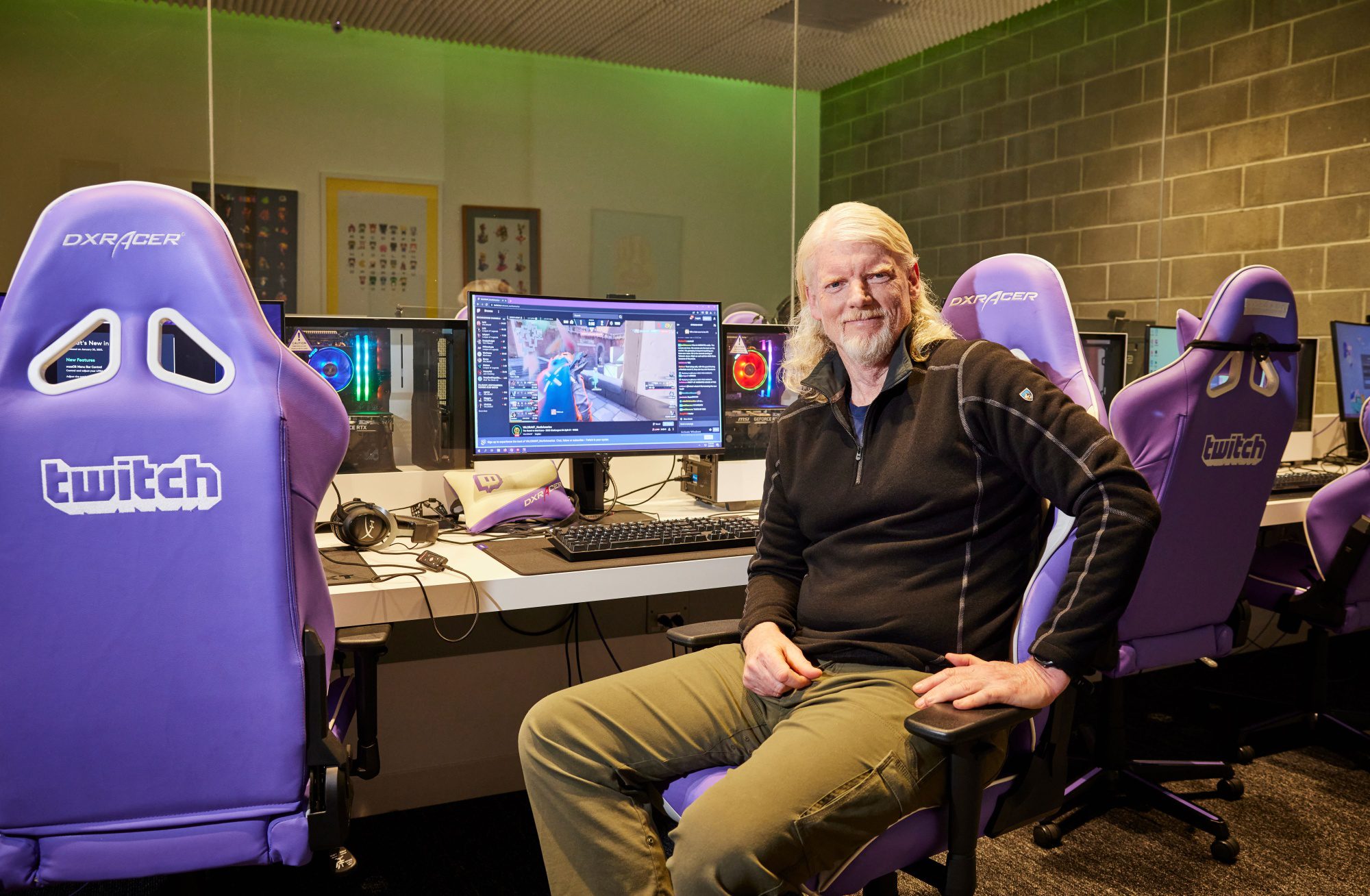 Dan Clancy Twitch CEO Dan Clancy seated in a purple gaming chair and smiling. Behind him is a monitor with an unknown Twitch stream active.