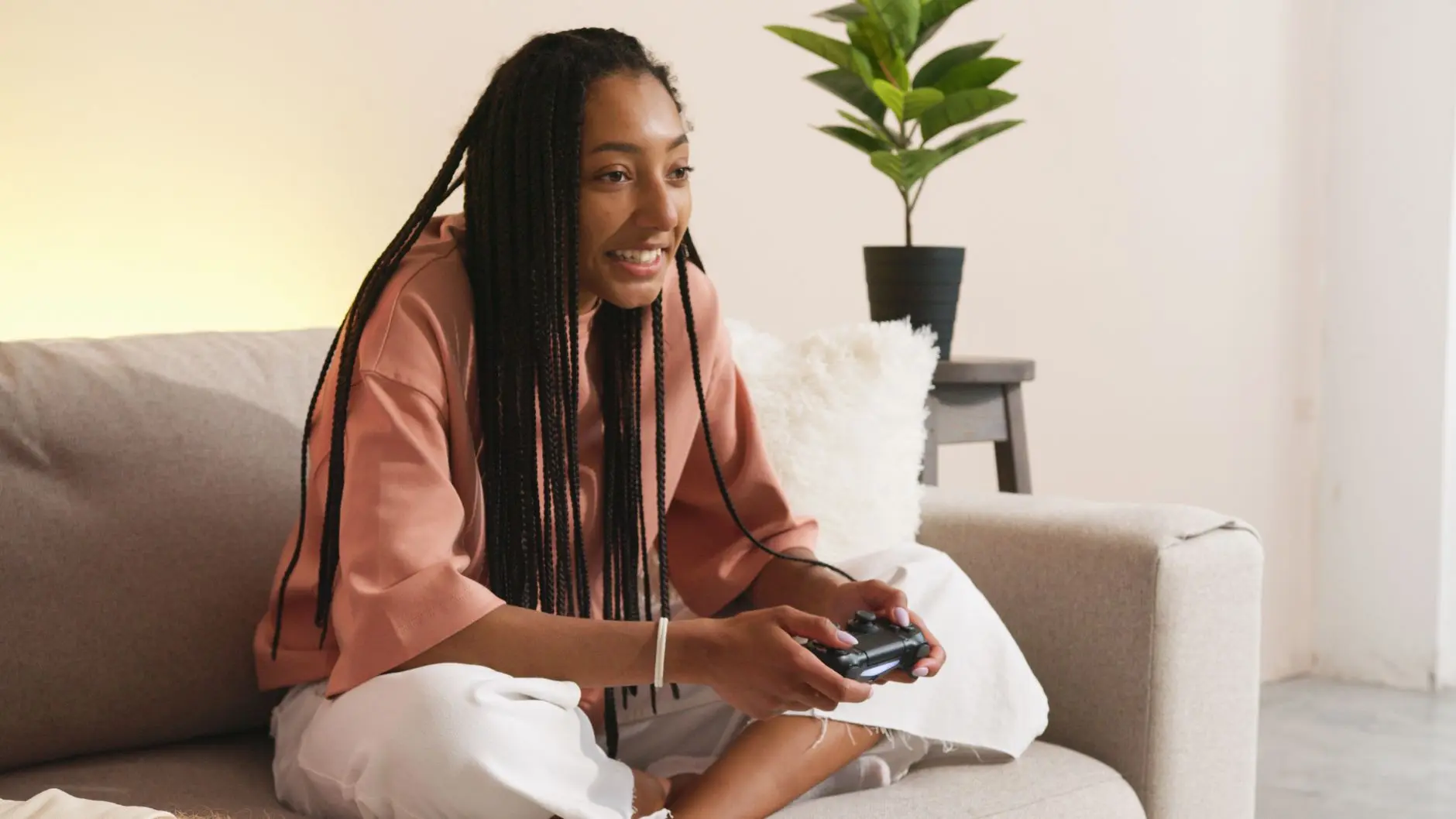 Person with braids relaxing on a couch, playing a video game controller.