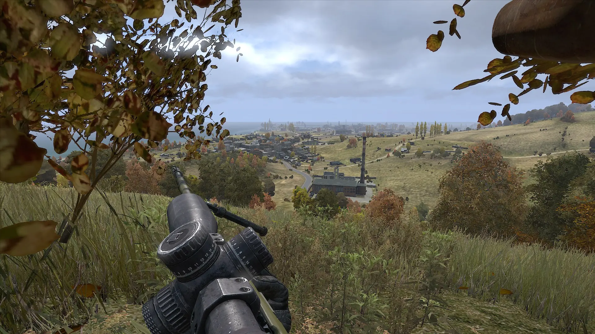 First-person view of a sniper rifle aiming at a town from a grassy hillside in DayZ