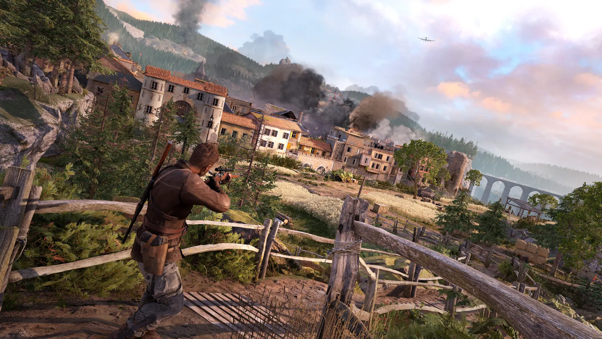 Third-person perspective of a sniper aiming a rifle at a smoking village in a mountainous landscape