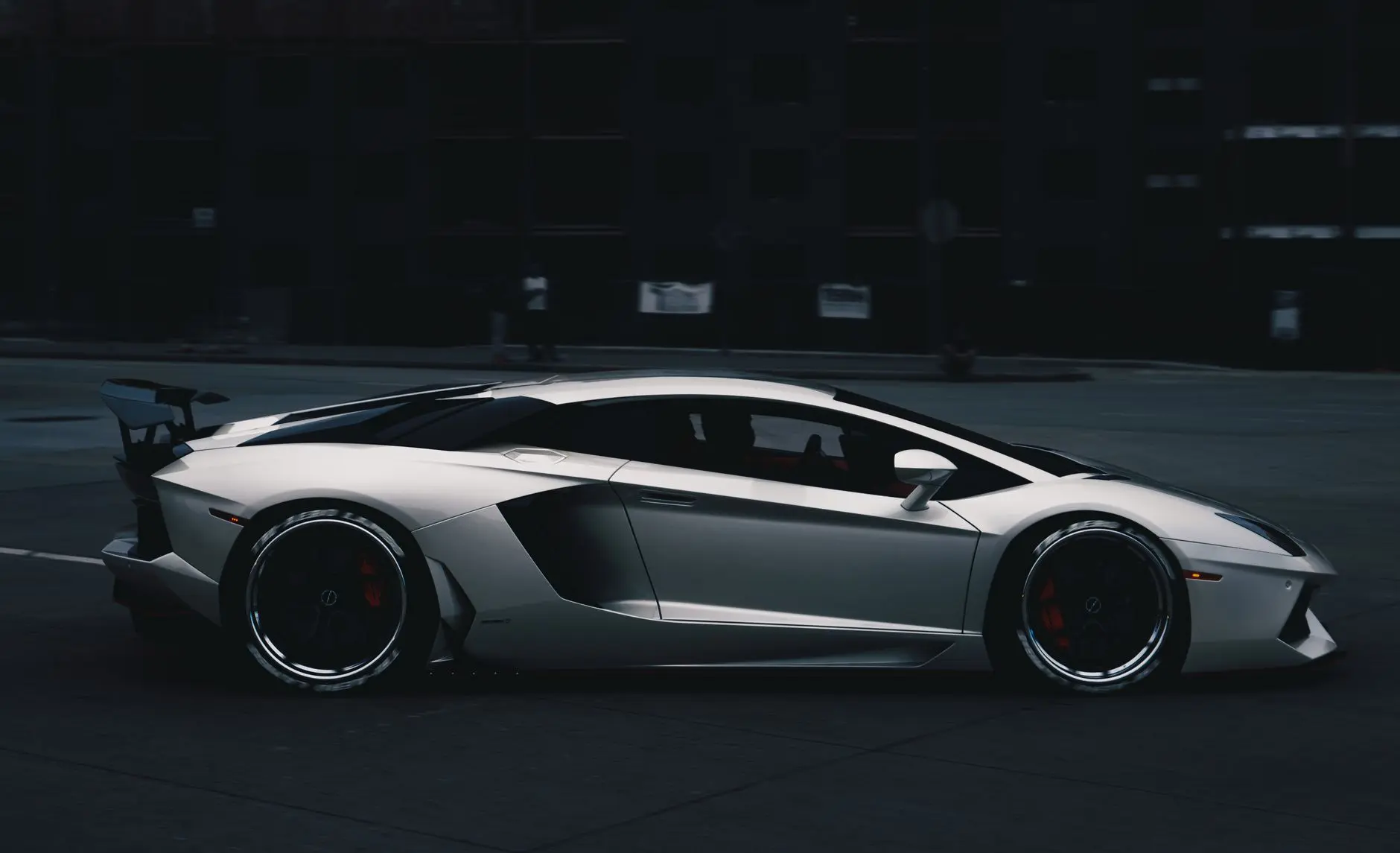 Side profile of a sleek white Lamborghini Aventador parked on a city street at night