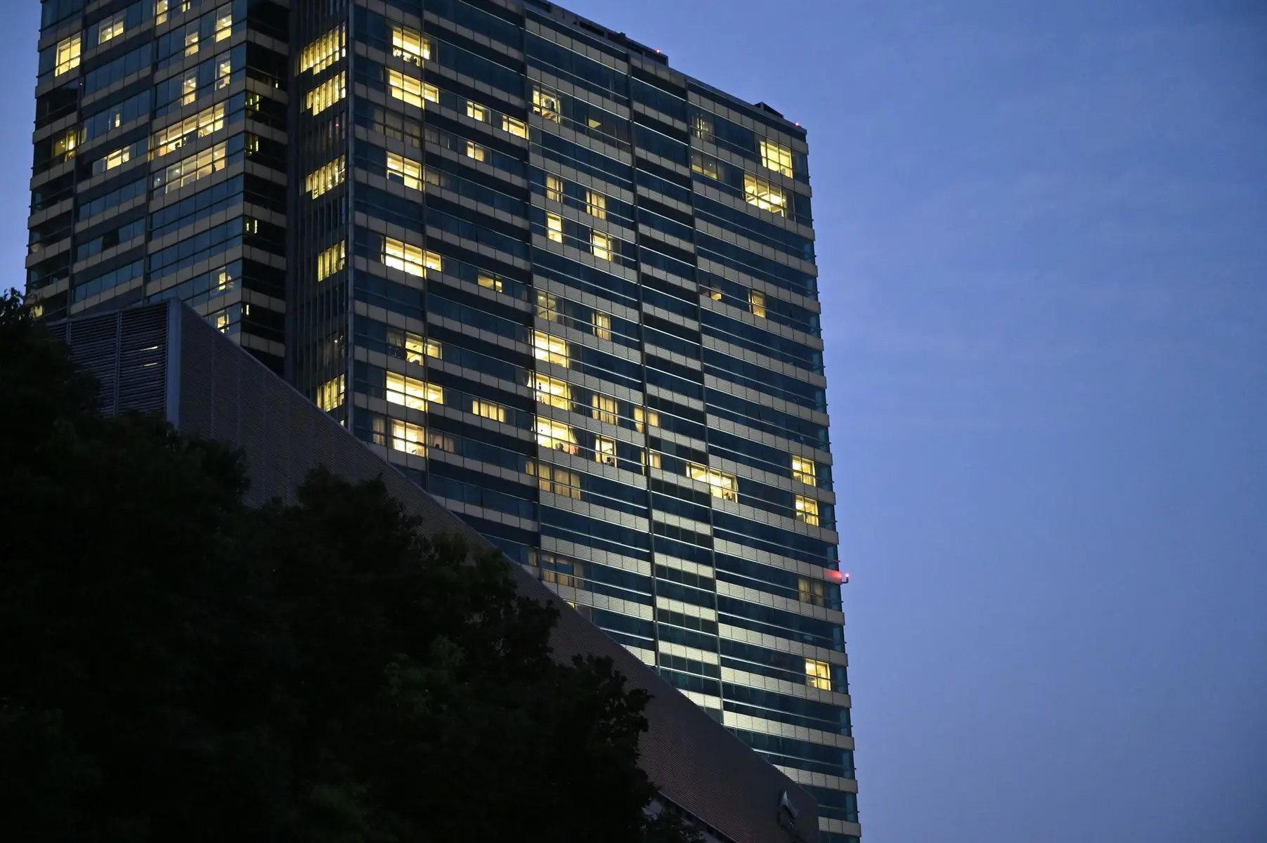 Low-angle view of a modern glass office building with illuminated windows at dusk