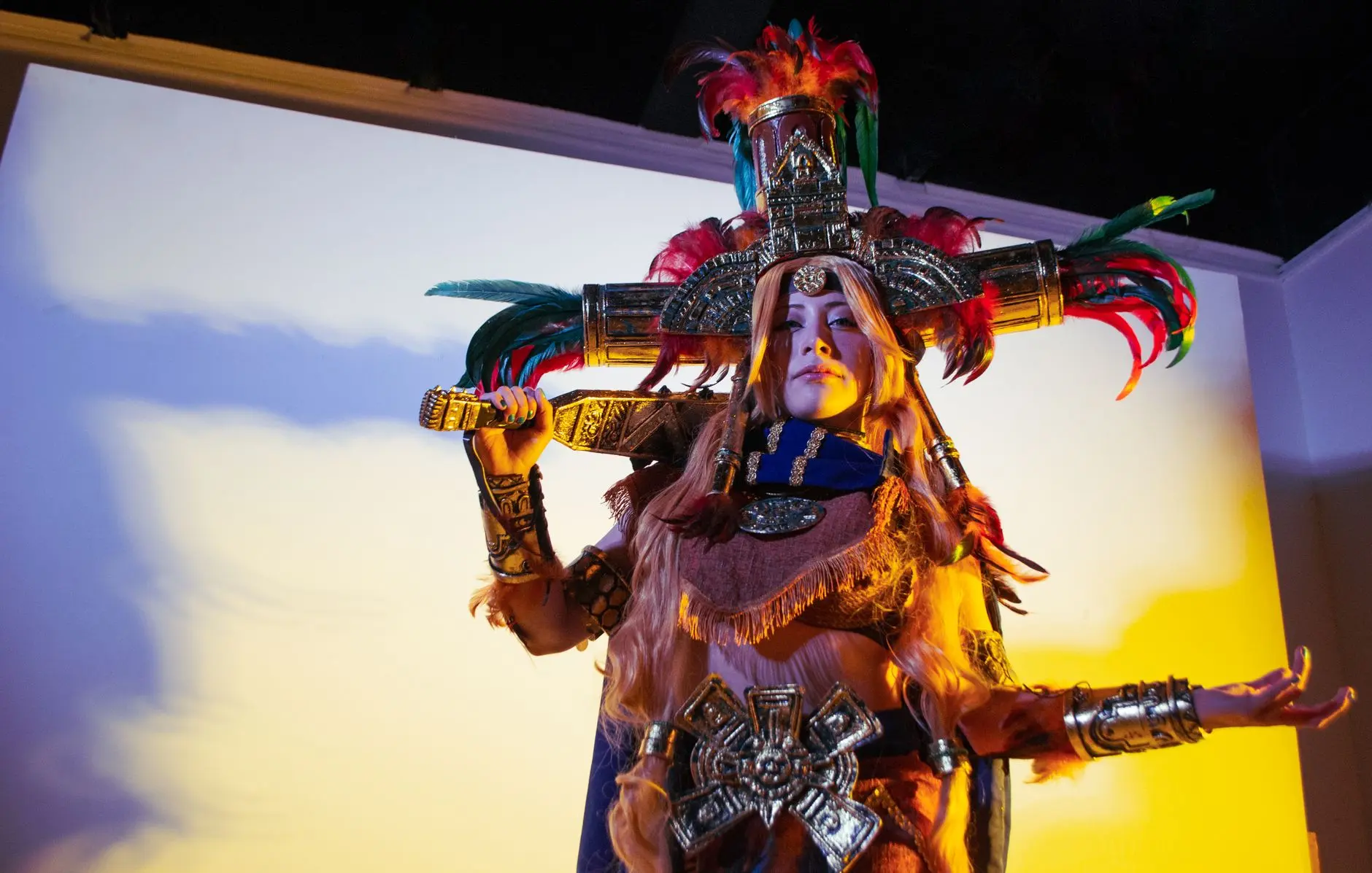 Cosplayer wearing an elaborate World of Warcraft inspired tribal outfit with a large feathered headdress